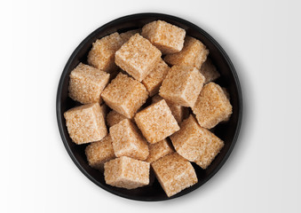 Black bowl plate of natural brown sugar cubes on white background.