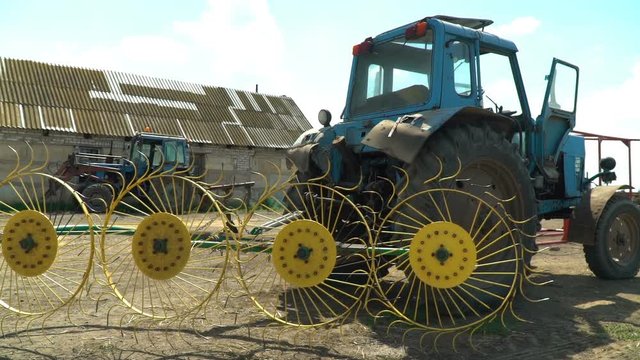 On a blue Soviet tractor are a rake of tedders and swaths