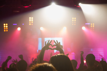 Crowd of unrecognizable fans joining hands in shape of hearts while expressing love in relation to performer at concert