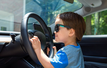Toddler boy in playing in the drivers's seat of his family's car in sunglasses