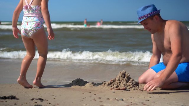 Fat father with hat and little playful daughter building castle from wet sand