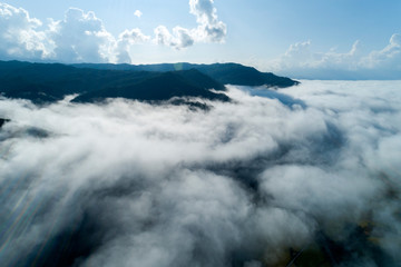 Aerial view drone shot of flowing fog waves on mountain tropical rainforest,Bird eye view image over the clouds Amazing nature background with clouds and mountain peaks