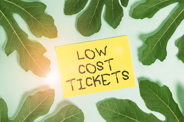 Conceptual hand writing showing Low Cost Tickets. Concept meaning small paper bought to provide access to service or show Leaves surrounding notepaper above empty soft pastel table