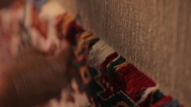 An elderly woman sews an oriental carpet. Handwork, a beautiful multi-colored carpet. Close-up of female hands that cleverly and quickly work behind a loom.