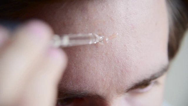 Man putting drop of serum on his forehead and rubs it with hand. Close up handled shot.