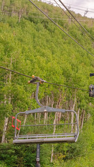 Fototapeta na wymiar Vertical Chairlifts on cables over ski mountain with thick green trees during off season