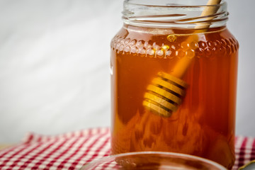 honey in glass jar with wooden dipper on white background