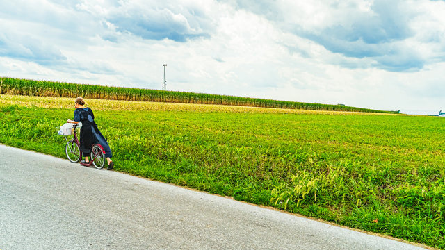 Amish young woman rides a scooter on road along the field field agriculture in Lancaster, PA US