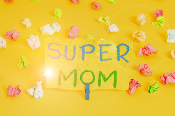 Handwriting text writing Super Mom. Conceptual photo a mother who can combine childcare and fulltime employment Colored crumpled papers empty reminder white floor background clothespin