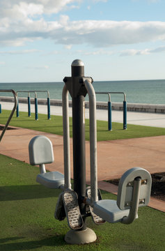 Exercise equipment in a public park on a sunny day with green ground cespe and sea in the background