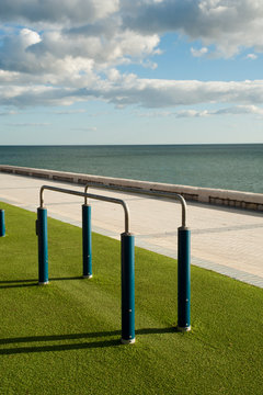 Exercise equipment in a public park on a sunny day with green ground cespe and sea in the background