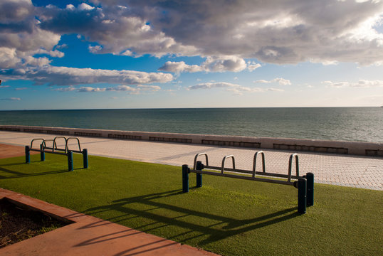 Exercise equipment in a public park on a sunny day with green ground cespe and sea in the background