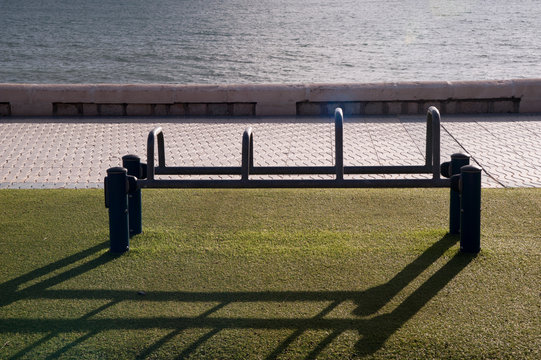 Exercise equipment in a public park on a sunny day with green ground cespe and sea in the background