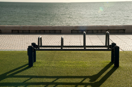 Exercise equipment in a public park on a sunny day with green ground cespe and sea in the background