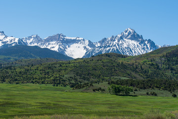 Fototapeta na wymiar Landscape of meadow, green hillside and snow dappled mountain tops near Ridgway, Colorado