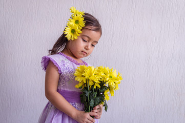 Little girl with yellow flowers in her hair, looks bouquet in her hands straight head