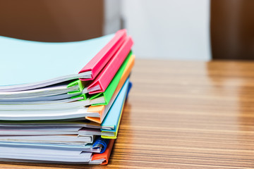 Pile of unfinished paperwork stacked in archive with plastic slide binder bars on office table waiting to be managed and inspected for score. Report papers stacks. Business and education concept.