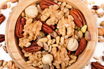 Pecan, macadamia, pistachio, pine nuts, walnuts in wooden bowl isolated on white background.