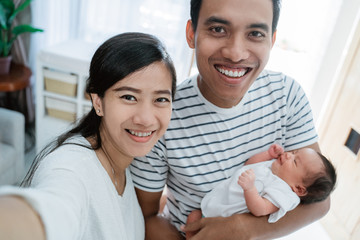 Selfie concept, cheerful family carrying little baby daughter at home