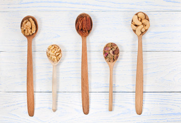 Pecan, cashew, pistachio, pine nuts, walnuts in wooden spoons on wooden background. Top view. Text space.