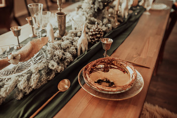 style Christmas table setting, gold plate and cutlery, on a wooden table and green cloth, with tree decorations
