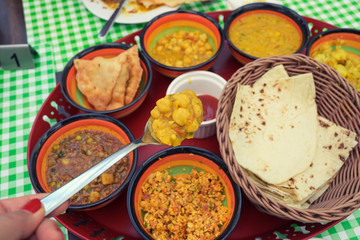 Traditional Bahrain breakfast curry soup in spoon of woman hand holding up in selective focus over group of middle east Bahraini food background on table.