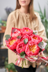 Mono bouquet of peonies, coral charm, in womans hands. Modern floral shop. Finished work of the florist. Delivery fresh cut flower from online store