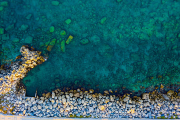 Aerial view of slide turn from drone on view of calm turquoise sea water and rocks from molten lava. Pattern of sea surface and rocky shore. Greece. Rocky coast