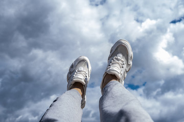 Young man walking in the clouds. Concept, white sneakers on a blue background with clouds