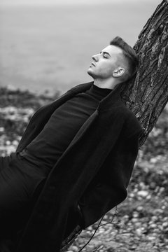 fashion male model in coat black and white photo, lies on tree, art portrait of man