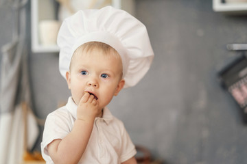 one little boy in hat of chef in kitchen sitting on the table and eat