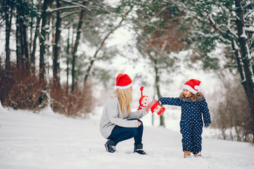Fototapeta na wymiar Family have fun in a winter park. Stylish mother in a gray sweater. Little girl in a red hat