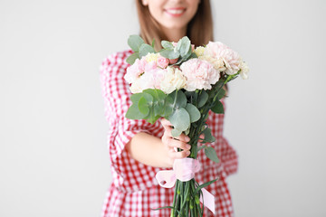Beautiful young woman with bouquet of carnation flowers on light background