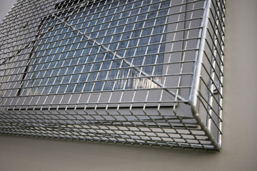 Window security wire mesh frame fixed externally to building wall to deter intruders 