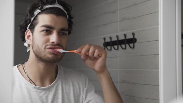 Bearded man brushing his teeth in front of mirror in bathroom