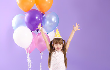 Happy little girl with Birthday air balloons on color background
