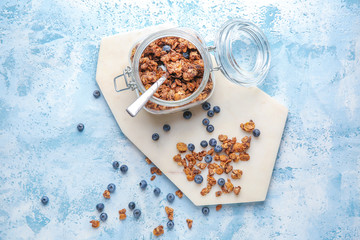 Jar with tasty granola and berries on color background