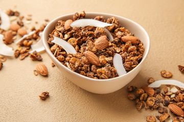 Bowl with tasty granola, coconut and almond on color background