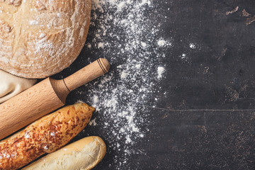 Different fresh bread with rolling pin on dark table