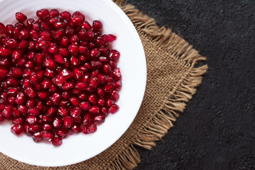  Pomegranate seeds are served in a white plate on a black background.