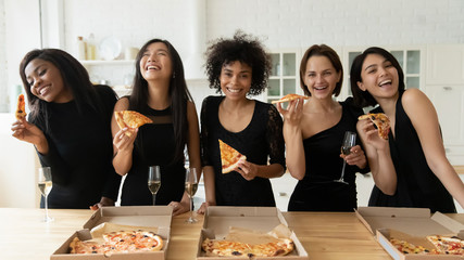 Happy diverse elegant women drink champagne eat pizza in kitchen