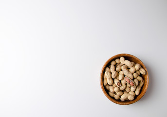 Unpeeled peanuts lies in a wooden bowl on a white background.