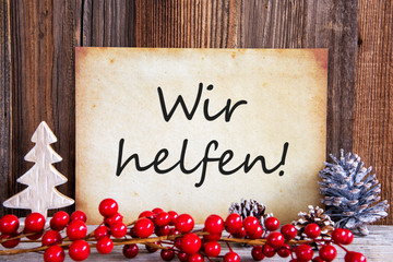 Fototapeta na wymiar Paper With German Text Wir Helfen Means We Help. Christmas Decoration And Wooden Background