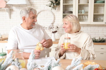 Happy mature couple having breakfast on Christmas eve in kitchen