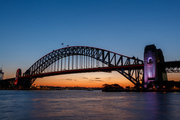 Illuminated Sydney Harbour Bridge viewed from Kirribilli at sunset