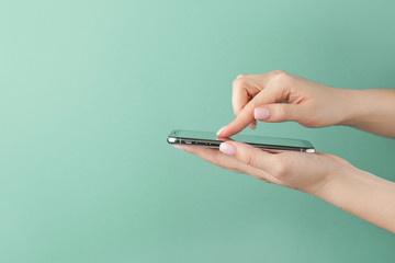 Female hands with modern mobile phone on turquoise background