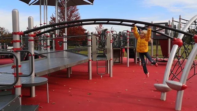 Young little Caucasian girl hanging climbing on monkey bar in park. Active preschool child doing exercises sport outdoor on playground. Healthy happy childhood.