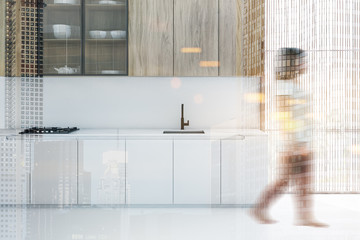 Woman walking in white kitchen with countertops