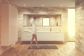Woman walking in light bathroom with sink