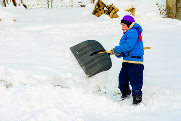 Little boy with big shovel removes snow after a snowstorm.